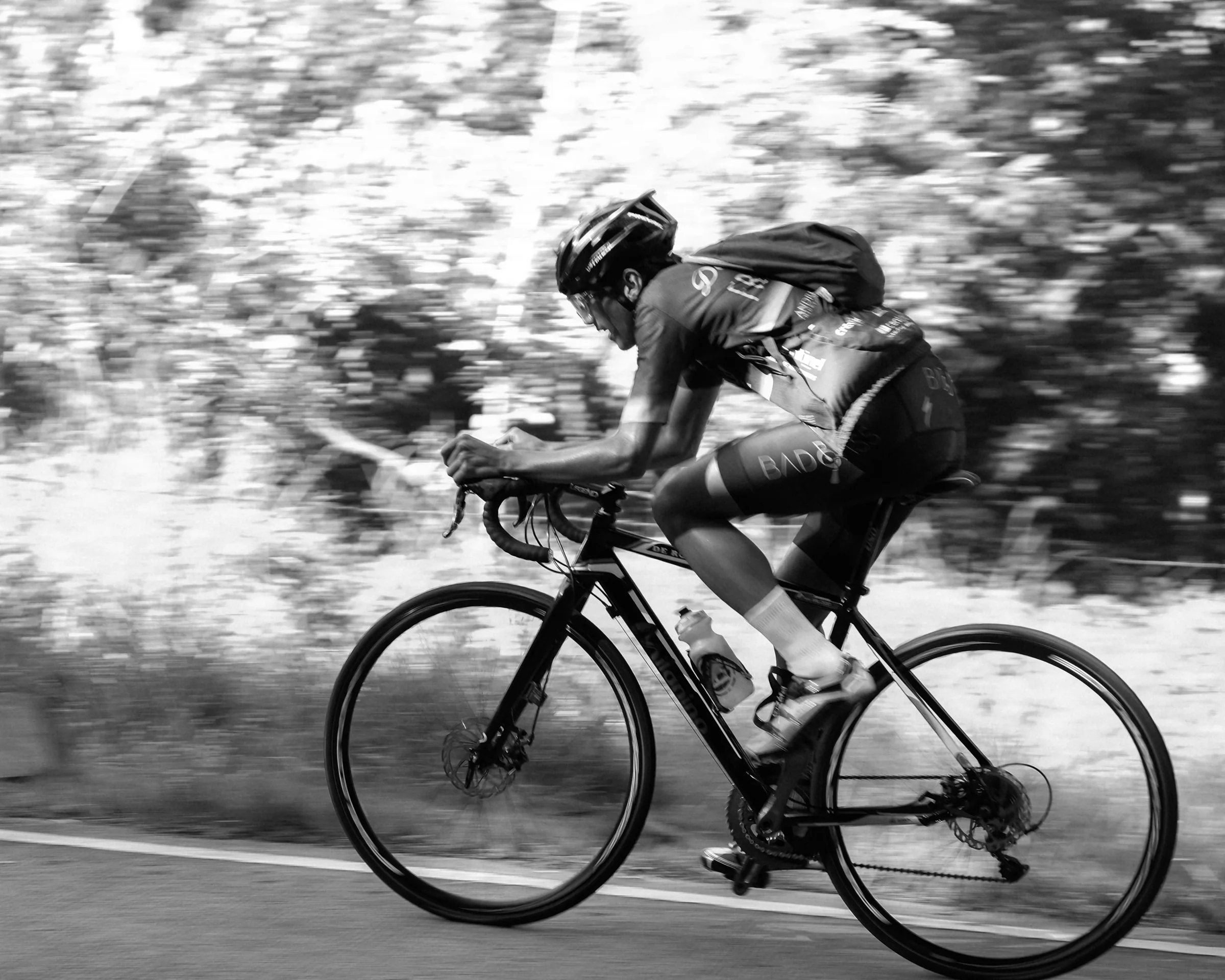 Black-and-white panning photograph of a road cyclist leaning low over the handlebars while climbing through the Sierra Madre mountains in Tanay, with the background streaked by motion blur.